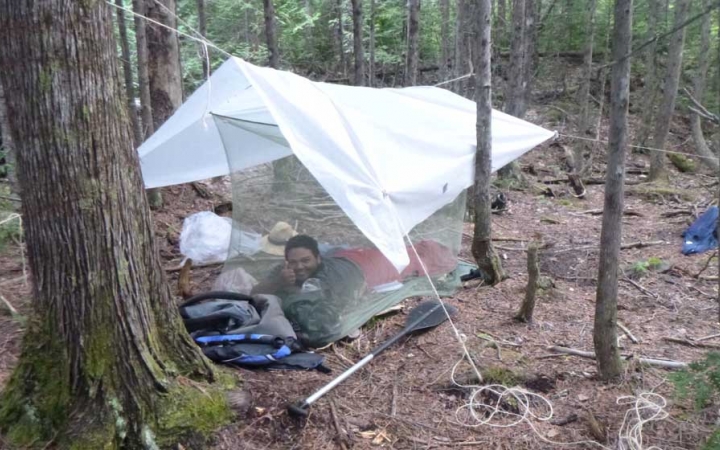 a person smiles while laying under a tarp in the woods on an outward bound expedition 